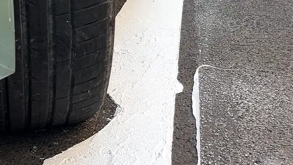 Die Markierung eines weißen Parkstreifens ist nicht komplett durchgezogen, weil ein Auto im Weg steht.