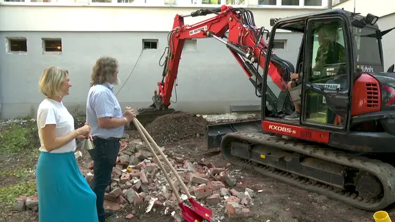 Eine Frau und ein Mann stehen neben einem Bagger