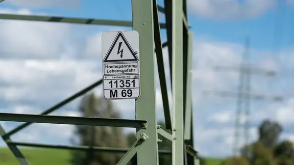 Ein Warnschild mit der Aufschrift Hochspannung Lebensgefahr kennzeichnet einen Bereich am Metallmast. Es dient der Sicherheit und warnt eindringlich vor den Gefahren durch Elektrizität.